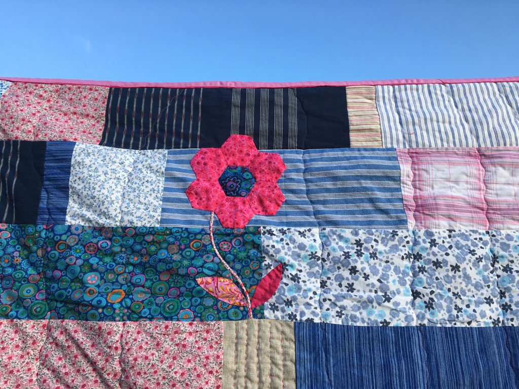 Detail: eine rosafarbene, applizierte Blume mit Stiel aus Liberty-Stoff.