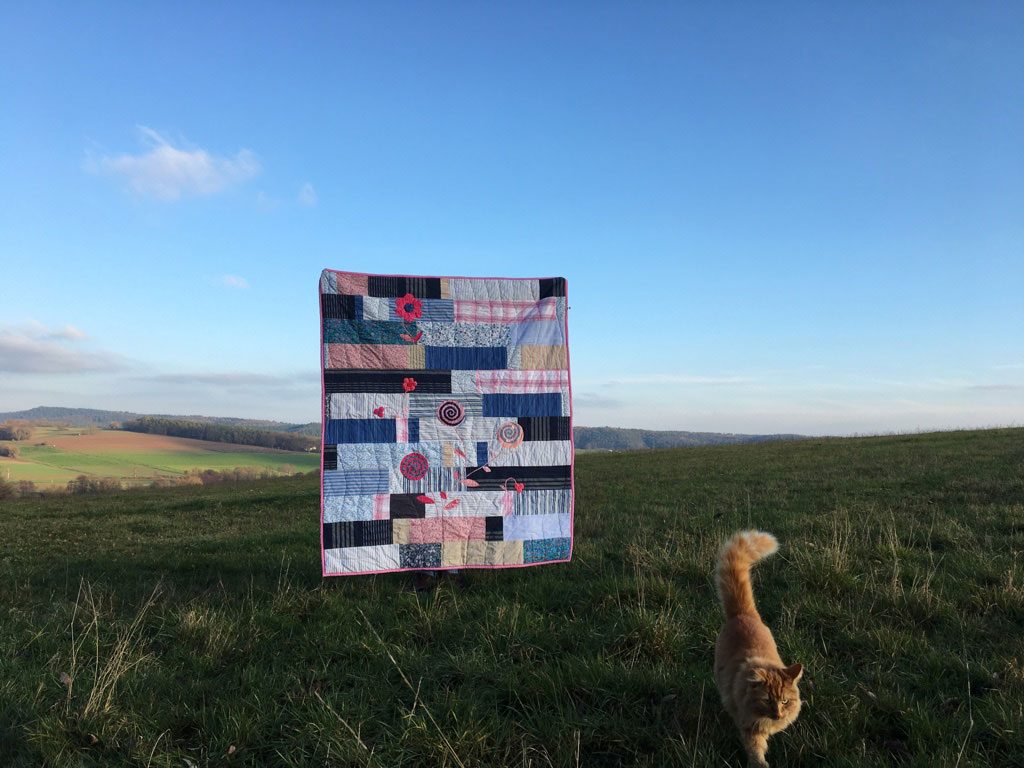 Evas Quilt hängt in einer weiten Landschaft, davor ein Hund im Gras.