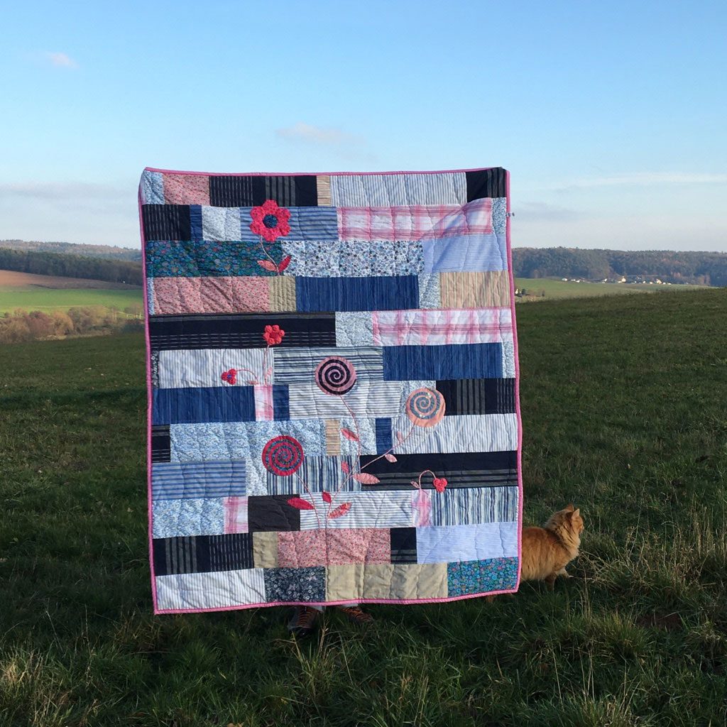 Eva’s Quilt hanging outdoors in front of fields and hills, with a meadow in the foreground.
