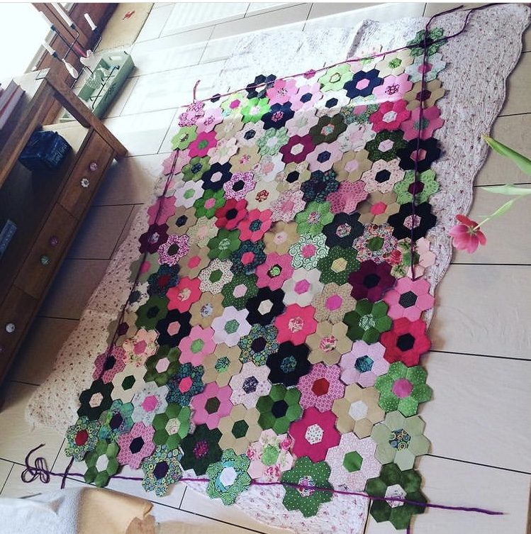 Lots of small hexagon flowers in pink, green and blue lying side by side on the floor.