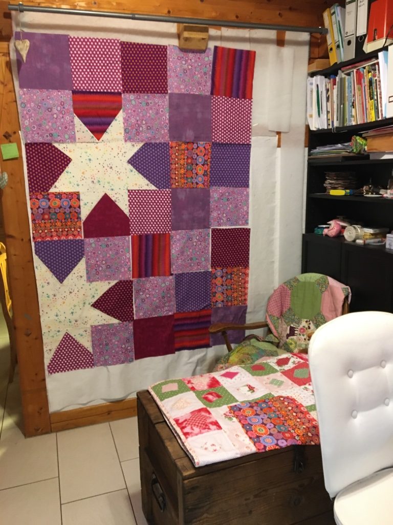 The finished star quilt hanging in front of bookshelves.