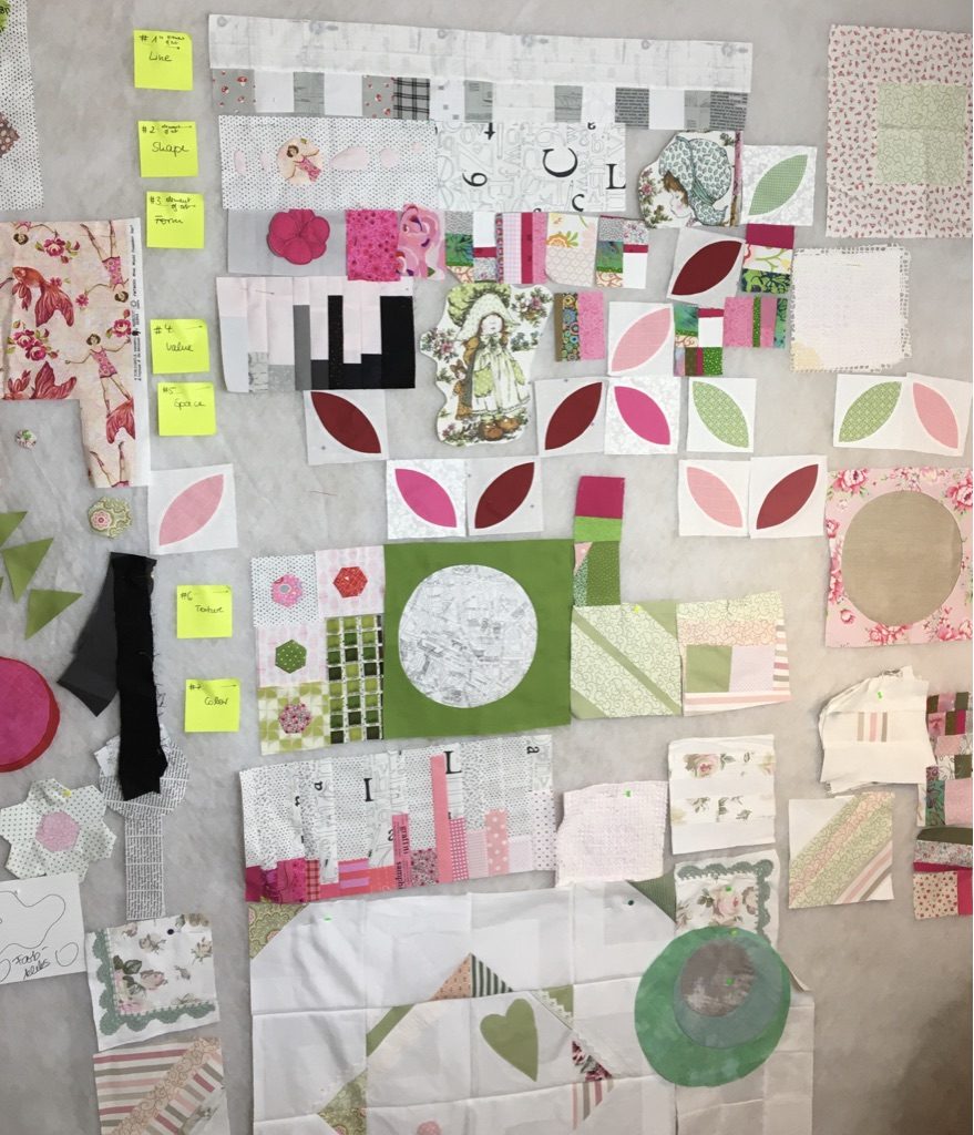 Lots of small fabric blocks of different sizes in pink, green and white on a gray design wall, with yellow notes in between.