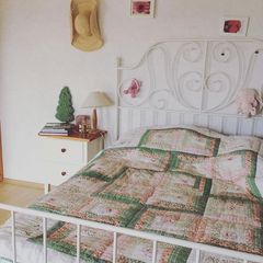A log cabin quilt in green and pink on a white metal bed in a bright bedroom.