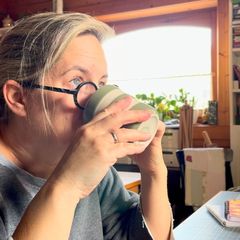 Caroline drinks from a mug in her sewing room.